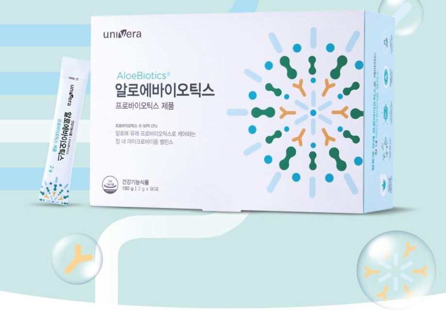 방울과 흰 곡선이 깔린 하늘색 지면 위의 알로에바이오틱스 패키지 상자(하늘색 옆면)와 그 앞의 스틱 1포. 상자 글자: univera, AloeBiotics®, 알로에바이오틱스, 프로바이오틱스 제품, 프로바이오틱스 수 50억 CFU, 알로에 유래 프로바이오틱스로 케어하는 장 내 마이크로바이옴 밸런스, 건강기능식품 180 g | 2 g x 90포