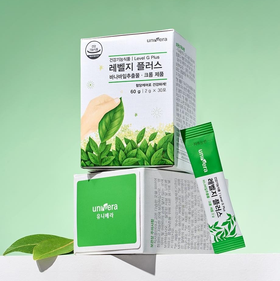 흰 받침대 위에 쌓인 레벨지 플러스 60 g 상자 두 개(건강기능식품 | Level G Plus · 바나바잎추출물 · 크롬 제품 · 혈당케어로 건강하게! · 60 g | 2 g × 30포)와 초록 스틱 하나, 잎 두 장
