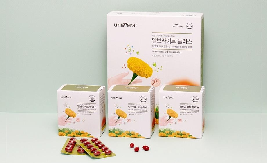 연녹회 벽 앞 알브라이트 플러스 큰 상자(건강기능식품 | Albright Plus · EPA 및 DHA 함유 유지 · 루테인 · 비타민A 제품 · 216 g)와 작은 상자 셋, 빨간 캡슐 블리스터 둘과 캡슐 셋